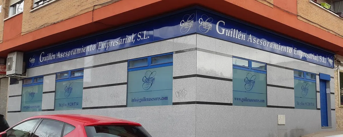 Esquina de nuestra oficina en la calle Reyes Católicos 17 de Móstoles, con el rótulo azul «Guillén Asesoramiento Empresarial, S.L.» sobre la fachada de granito